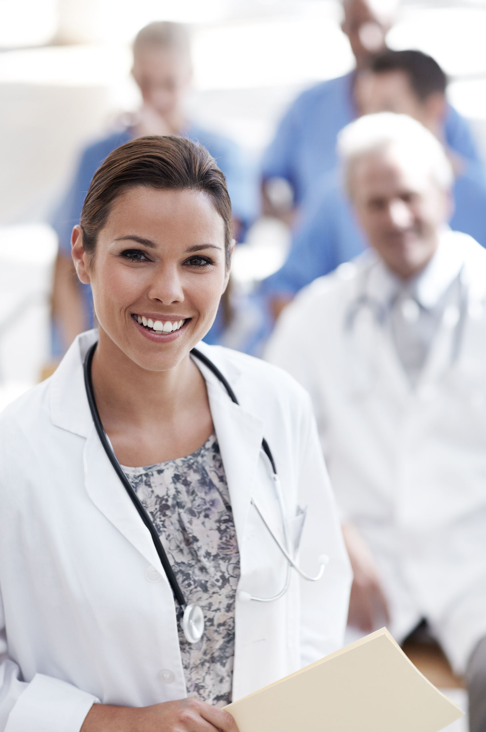 A doctor standing with colleagues sitting in the background.